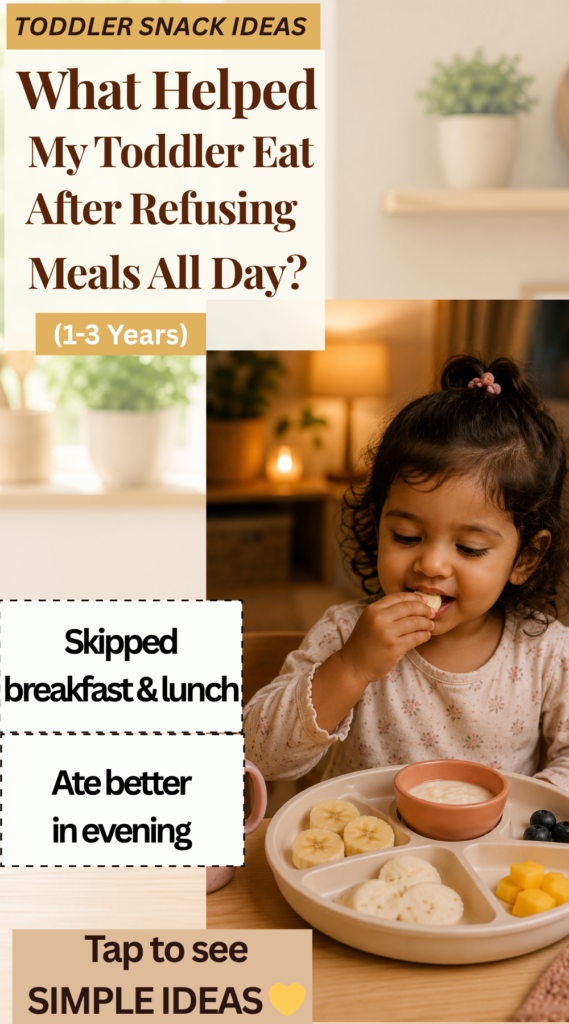 Toddler eating a small evening snack at dining table after refusing meals earlier in the day in a warm neutral kitchen setting.